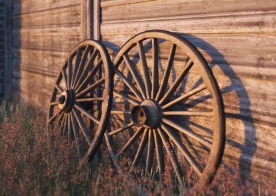 A closeup image of some cart wheels leaning against a fence in a rural setting